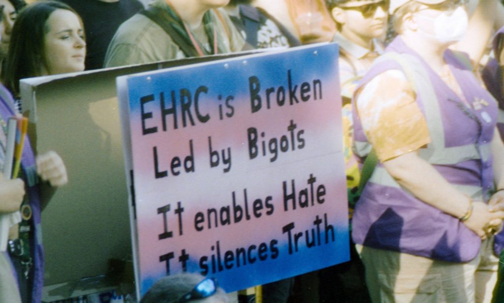 Someone holding a sign at a protest that reads "EHRC is broken led by bigots, it enables hate, it silences truth."