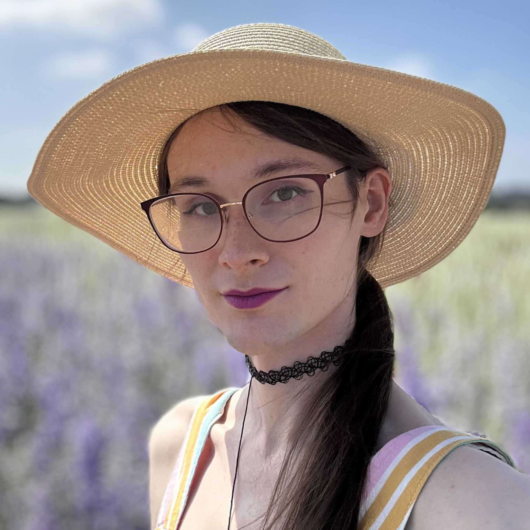 Sammi is pictured wearing a straw hat on a summers day, she has long straight brown hair and thin frame glasses on, she is looking directly at the camera