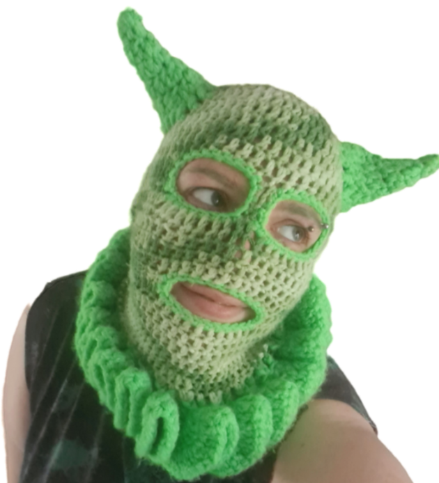 Flint, a white transmasc person with green eyebrows, pictured in a crochet green clown-balaclava, that that horns, wearing a green and black tshirt with ripped off sleeves, he is looking off to the left, Just like his politics.